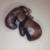 Gants de boxe marron vintage, cuire pleine fleur patiné à la main. Garnissage en fibres naturel, fermeture : lacet en coton. Élégante et stylée, cette paire de gants de boxe vintage fabriquée à l'ancienne servira à donner un aspect authentique à votre décoration. 